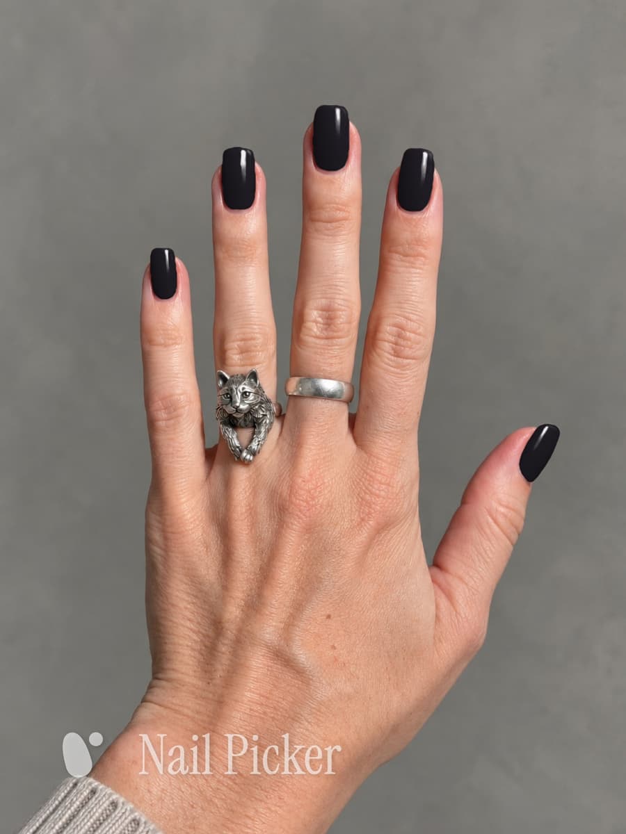A hand on a grey backdrop, nails painted a glossy, deep onyx black.
