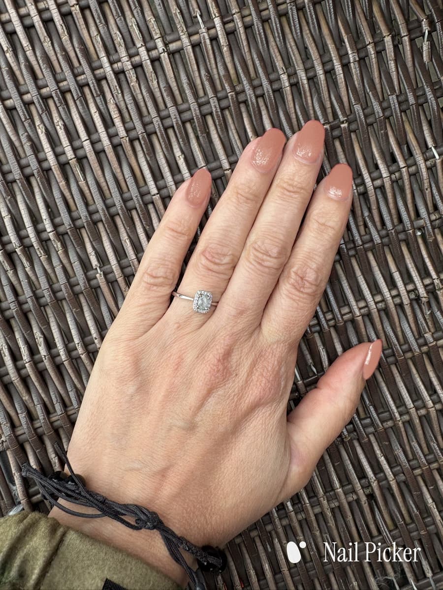 A hand lying on woven cane, nails in a warm terracotta nude with a soft sheen.