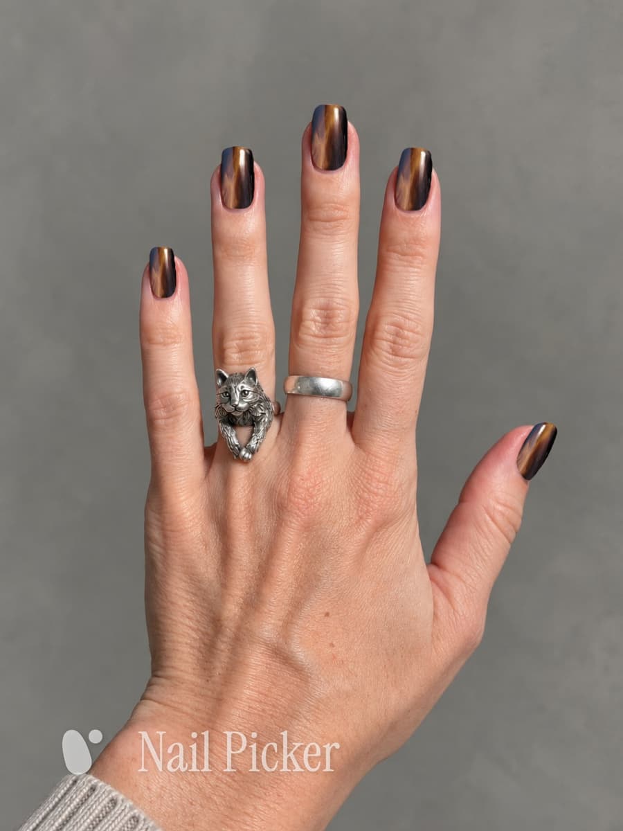 The same hand, nails in a tiger-eye finish — brown, gold and black moving together in each one.